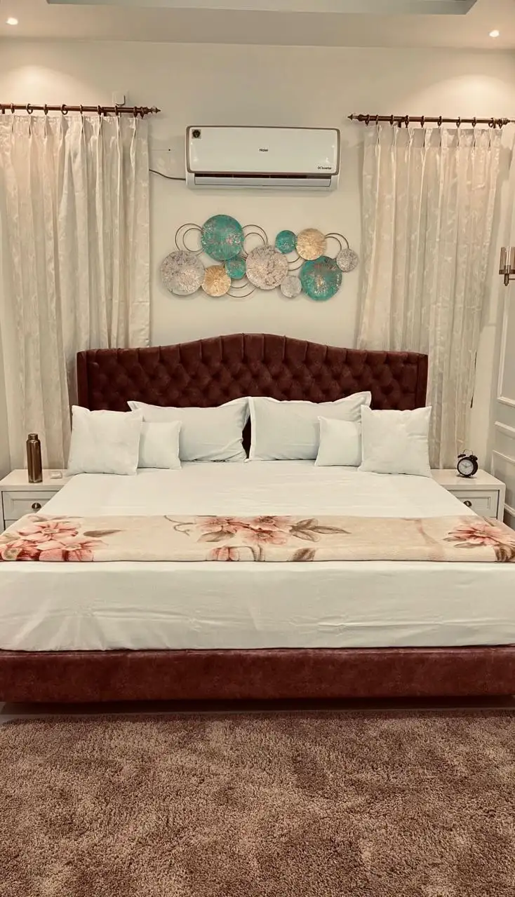 A beautiful modern bedroom with a tufted headboard, elegant curtains, and stylish wall décor, showcasing the expertise of an Interior designing company in Malappuram.
